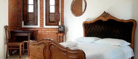 A bedroom with a wooden bed, a desk, and two windows with shutters.