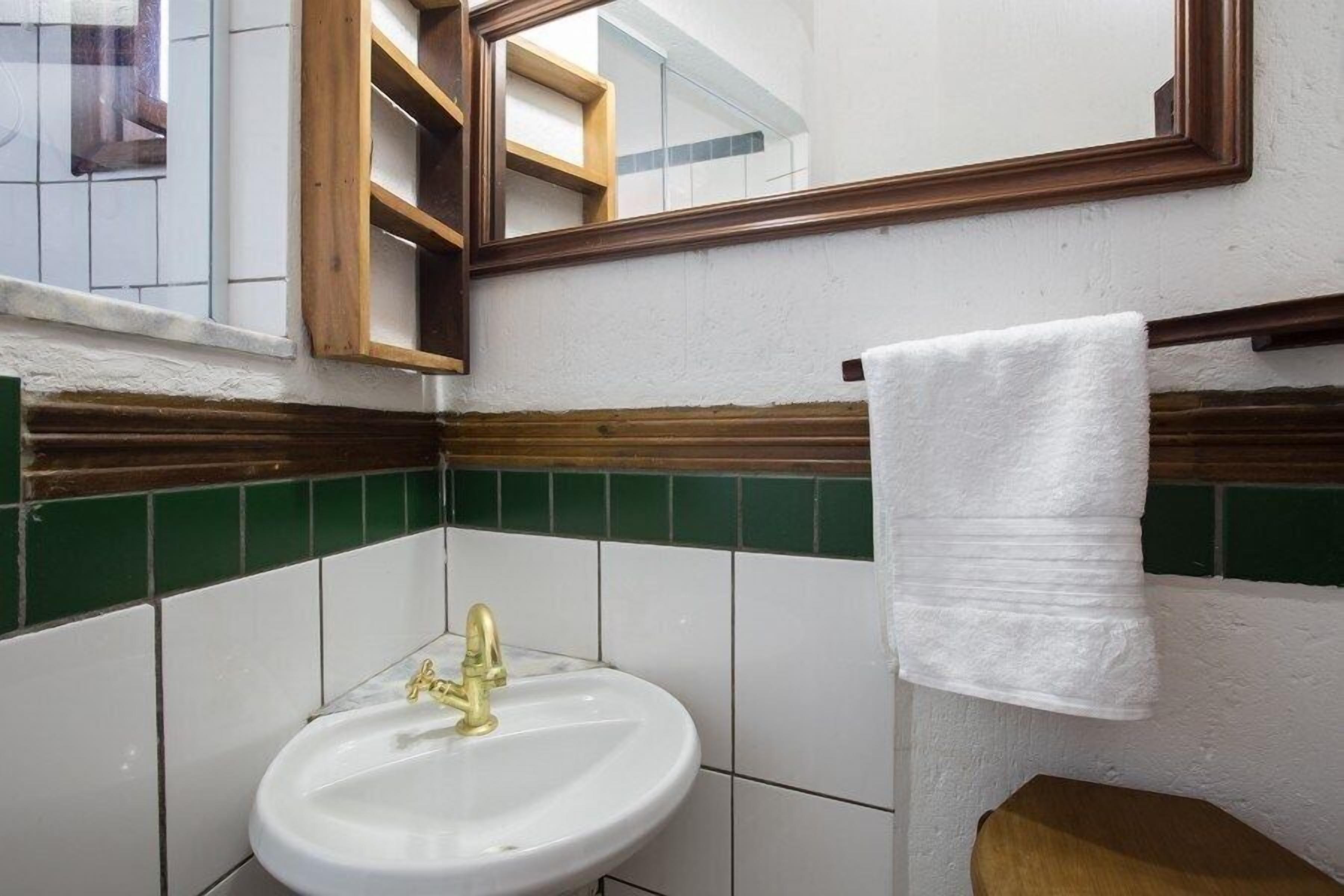 A bathroom with a white sink, gold faucet, and a mirror above it.