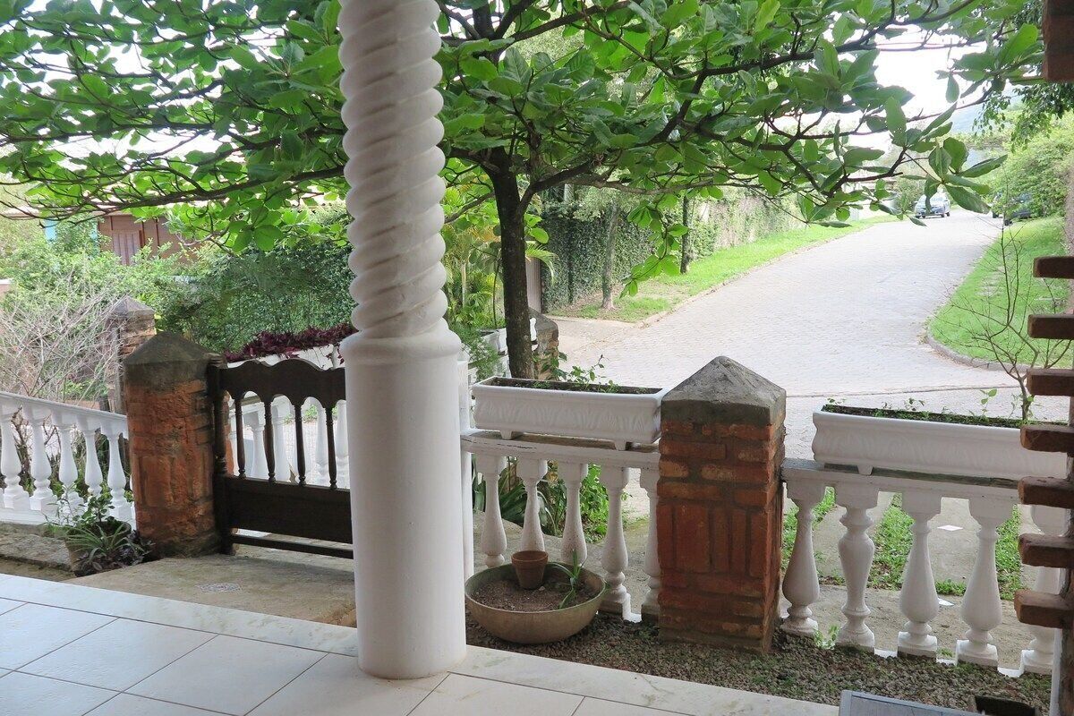 A covered outdoor area with a white balustrade, a potted plant, and a view of a road.