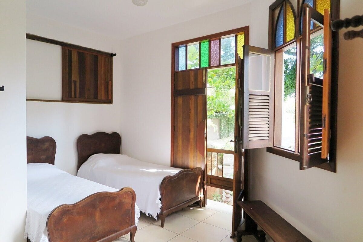 Ein Zimmer mit zwei Holzbetten, einer Bank, einem Fenster mit Fensterläden und einem an der Wand befestigten Regal.