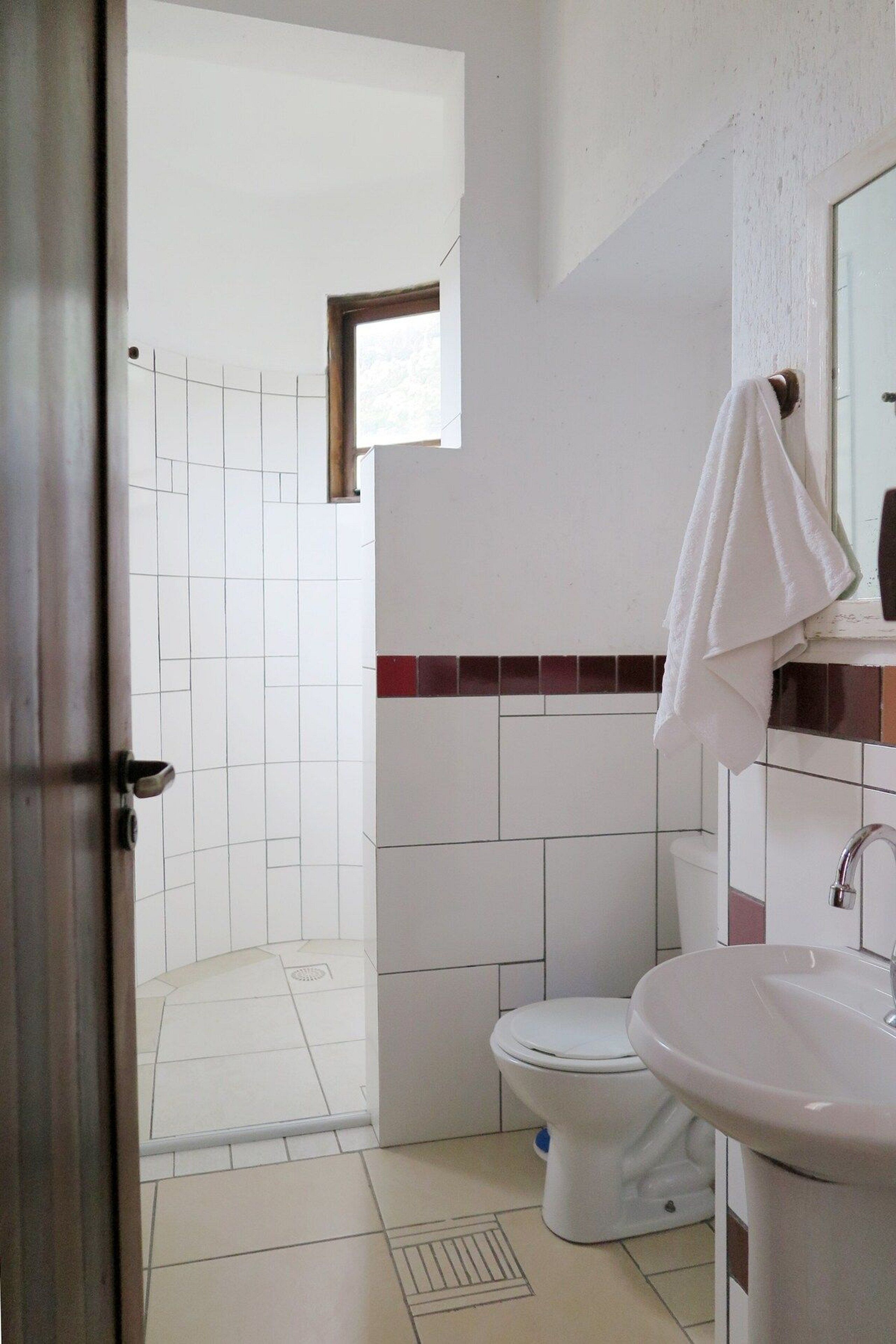 Un baño con inodoro blanco, lavamanos y zona de ducha.