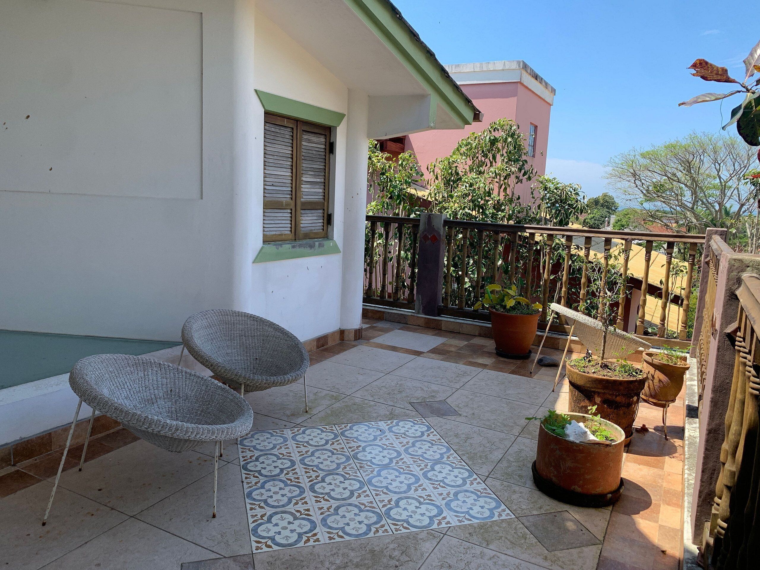A balcony with wicker chairs, potted plants, and a patterned floor.