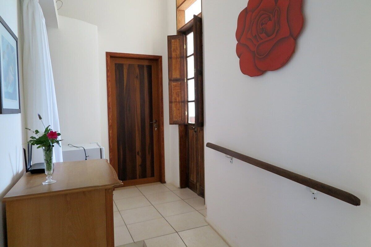Un pasillo con una puerta de madera, una pared blanca decorada con una rosa roja y un pequeño escritorio de madera con un jarrón de flores.