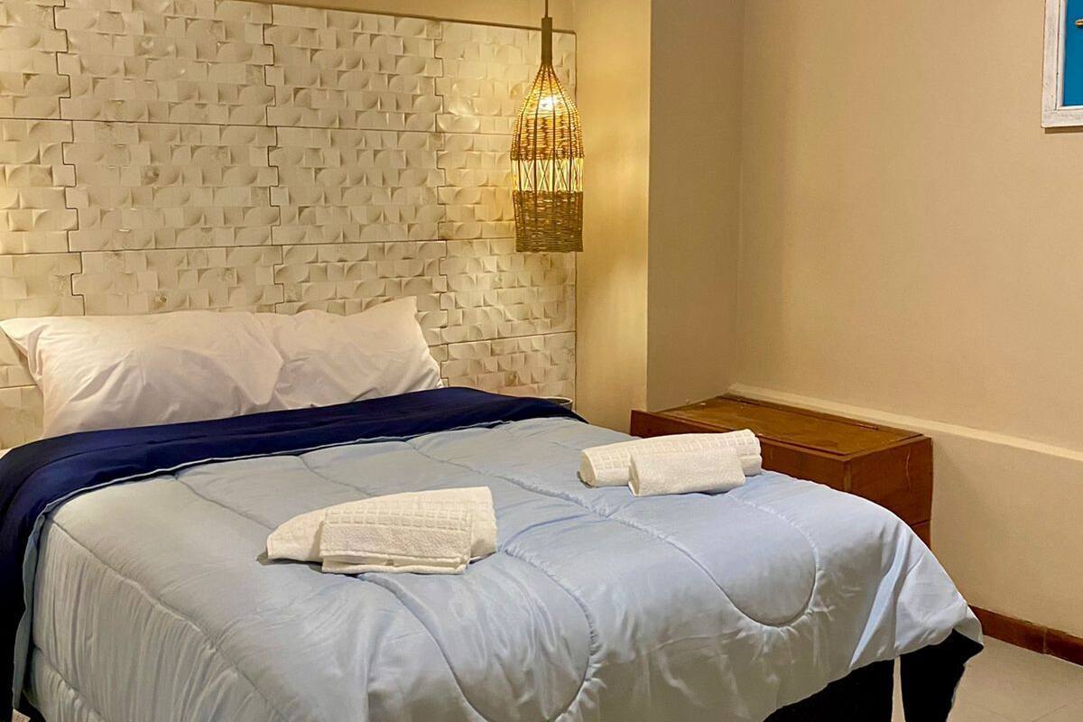 A modern bedroom with a patterned headboard, a bed with white linens, and a hanging light fixture.