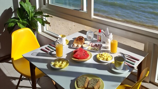 A breakfast table with a view of the sea and boats, a yellow chair, and a potted plant. - Sabatico Beach House (Búzios)