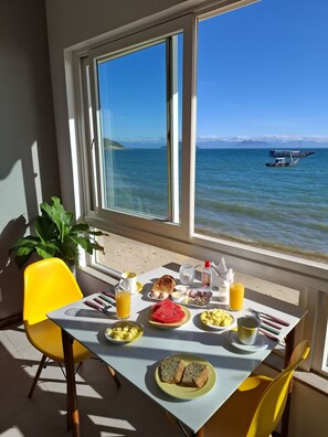 Ein Frühstückstisch mit Blick auf das Meer und Boote, ein gelber Stuhl und ein Blumentopf.