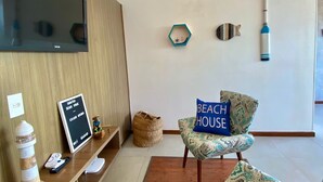 A modern living room with a wooden TV stand, a patterned armchair, and a wall-mounted TV. - Sabatico Beach House (Búzios)