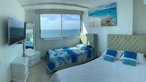 Un dormitorio con una cama grande, otra más pequeña, un televisor y una ventana con vista al mar.