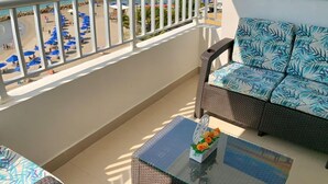Un balcón con vistas a la playa, un sofá, una mesa de centro y un cuadro.