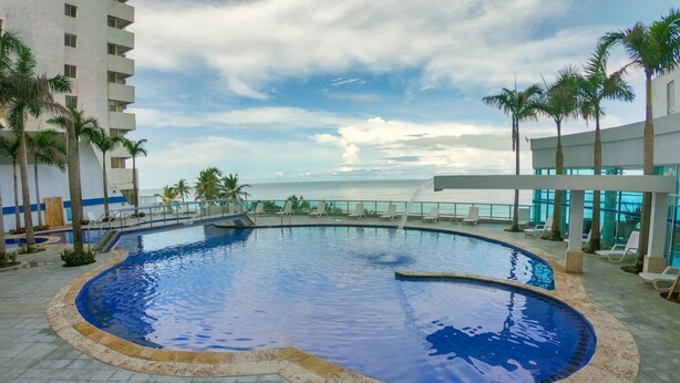 Una piscina con vista al océano, rodeada de palmeras y sillas de descanso.