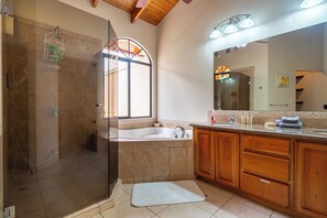 Un bagno con box doccia in vetro, una vasca da bagno indipendente, mobili contenitori in legno e un grande specchio.