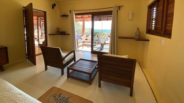A room with two wooden chairs, a small table, a view of the outdoors through a sliding door, and a hammock on the balcony.