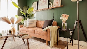 A cozy living room with a green wall, a brown sofa, a coffee table, and a floor lamp. - Bright! King bed *private office*terrace*gym* (Montréal)