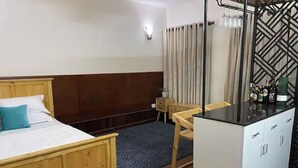 A hotel room with a wooden bed, a small desk with a chair, a minibar, and a window with curtains. - MAKACH House, Studio Apartment !! (Kathmandu)