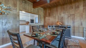A dining area with a wooden table set for six, surrounded by chairs. A kitchen with white cabinets and a microwave is visible in the background. - Spacious bohemian canyon home with views (Reno)