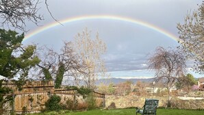 A garden with a wooden fence, a chair, and a rainbow in the background. - Spacious bohemian canyon home with views (Reno)