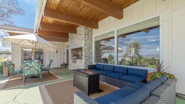 A covered outdoor seating area with a stone fireplace, blue sofa, and a fire table. - Spacious bohemian canyon home with views (Reno)