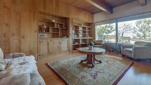A spacious living room with wooden walls and a large window, a round coffee table, and a sofa. - Spacious bohemian canyon home with views (Reno)
