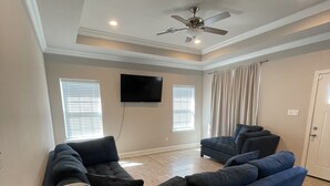 A living room with a sectional sofa, a ceiling fan, and a flat-screen TV mounted on the wall.