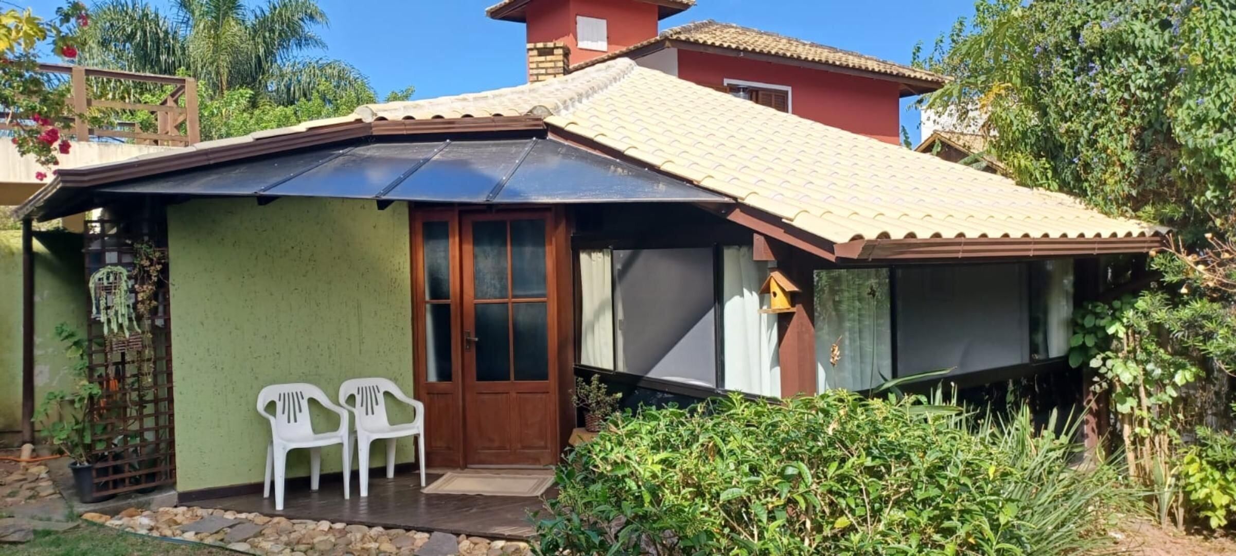 Uma casa com telhado de telhas, uma porta da frente e duas cadeiras de plástico brancas na parte externa.
