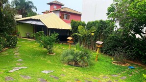 A pathway leading to a house with a tiled roof, surrounded by lush greenery and a small bird feeder. - Loft's Jardim's - Campeche - Floripa (Florianópolis)