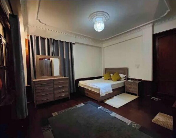 A bedroom with a bed, a dresser, a mirror, and a ceiling light. - Makach House, Condo With Beautiful Garden (Kathmandu)