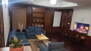 Ein Wohnzimmer mit einer Sofagarnitur, einem Couchtisch, einem Fernseher und einem Bücherregal.