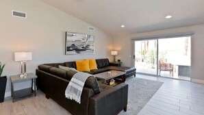 A modern living room with a sectional sofa, two side tables with lamps, a coffee table, and a large window with a view of the outdoors. - Luxury Getaway - Casa Vaugeois (Palm Desert)