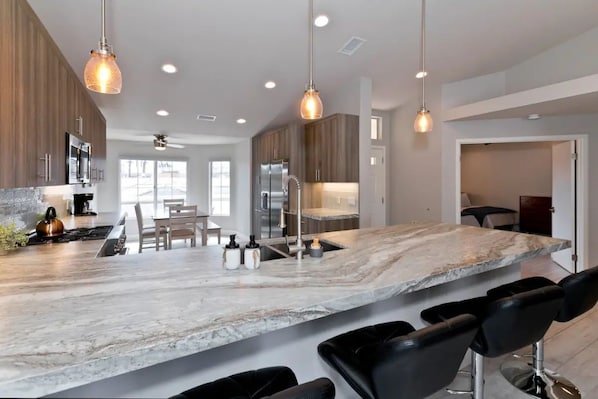 A modern kitchen with a marble island, bar stools, and pendant lighting.