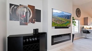 A modern living room with a black entertainment unit, a flat-screen TV mounted on the wall, and a fireplace. - Luxury Getaway - Casa Vaugeois (Palm Desert)