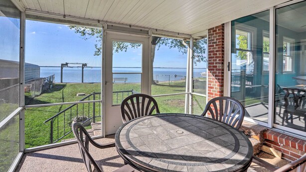 A covered patio with a table and chairs, overlooking a grassy area and a body of water. - Lakefront Cottage w/ Fishing & Private Yard! (Port Clinton)