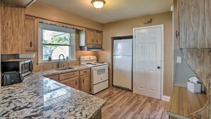 A kitchen with wooden cabinets, a granite countertop, a stove, a refrigerator, and a window with a view of the outside. - Lakefront Cottage w/ Fishing & Private Yard! (Port Clinton)