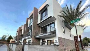 A modern multi-story building with a flat roof, large windows, and a balcony.