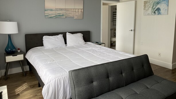 Un dormitorio ordenado con una cama grande, una mesita de noche con lámpara, un banco y un cuadro en la pared.