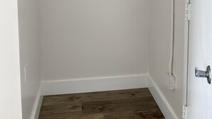 Un baño con una puerta blanca, piso de madera, un perchero con toallas dobladas y un estante con un rollo de papel higiénico.