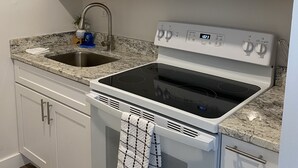 Una cocina con armarios blancos, un fregadero de acero inoxidable, un microondas, un horno y una placa de cocina.