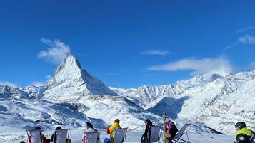 Un grupo de personas sentadas en sillas en un espacio exterior nevado, con una montaña al fondo.