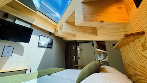 A room with a skylight, wooden ceiling, a bed with pillows, a flat-screen TV, and a framed picture on the wall.