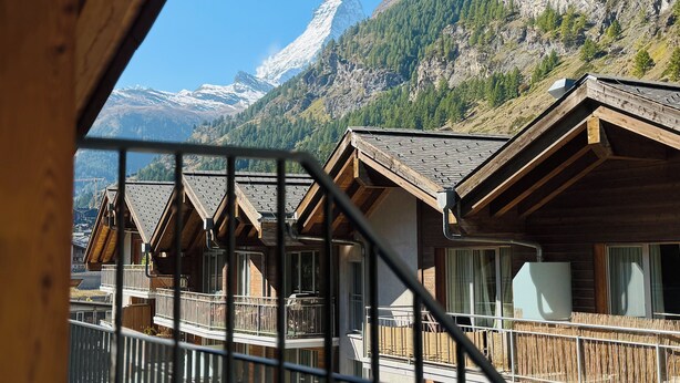 A mountain lodge with wooden cabins, a balcony, and a view of snow-capped mountains.