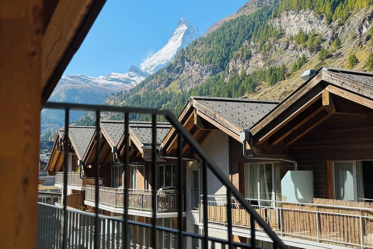 A mountain lodge with wooden cabins, a balcony, and a view of snow-capped mountains.