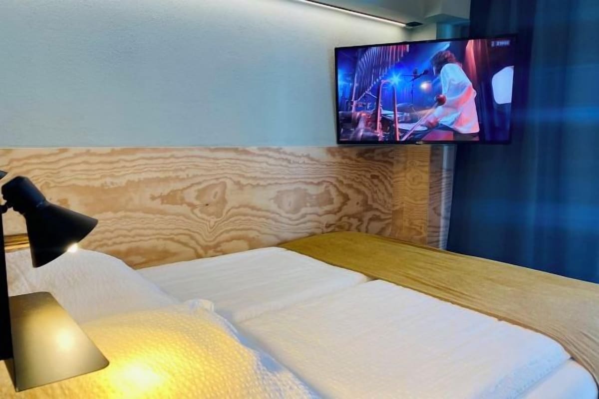 A hotel room with a bed, a television mounted on the wall, and a lamp on the side table.