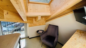 A room with a skylight, a chair, a small table, and a TV mounted on the wall.