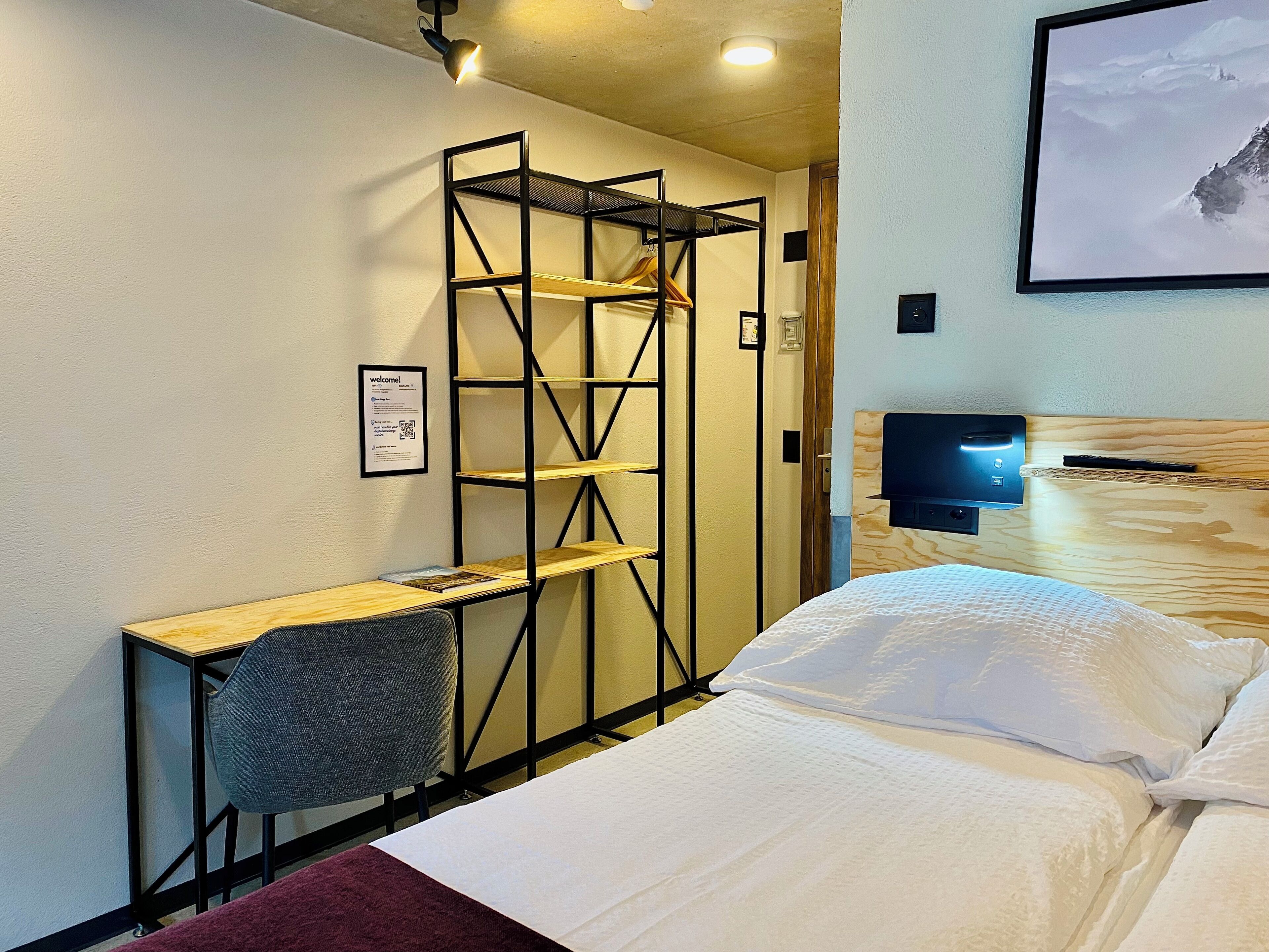 Habitación de hotel con cama, escritorio, silla, armario y televisión de pantalla plana.