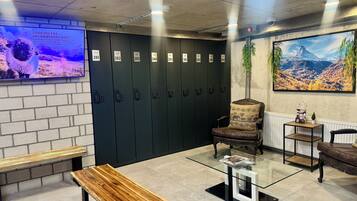 A reception area with lockers, a bench, a glass-top table, a chair, and a wall-mounted TV.