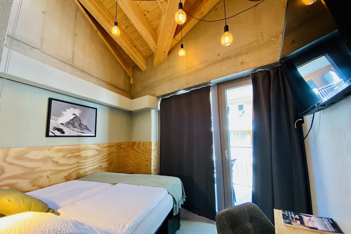 A room with a bed, a chair, a TV, and a window with curtains.