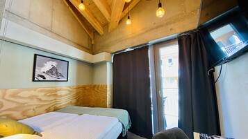 A room with a bed, a chair, a TV, and a window with curtains.
