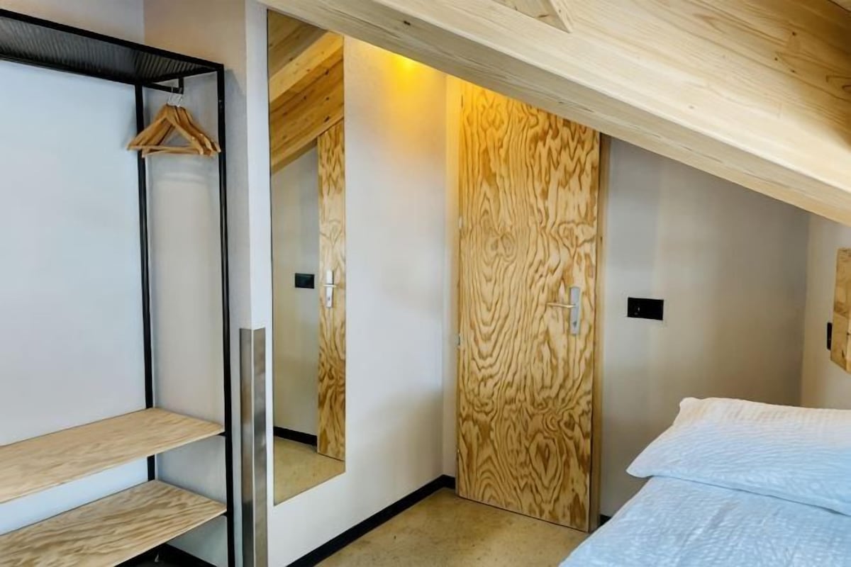 A bedroom with a bed, a wooden wardrobe, a mirror, and a hanging rack.