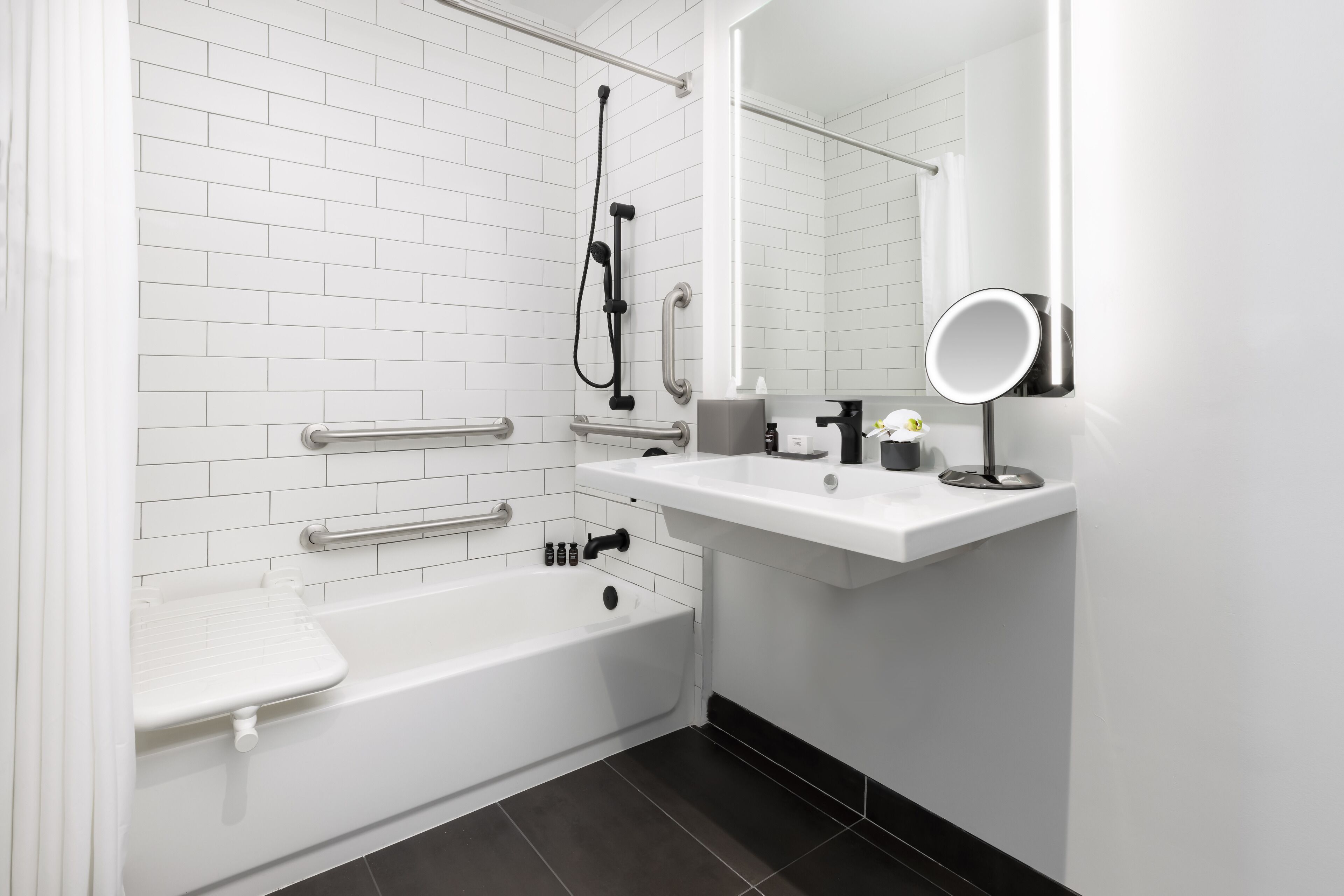 A modern bathroom with a white bathtub, a shower, a vanity with a mirror, and a toilet.