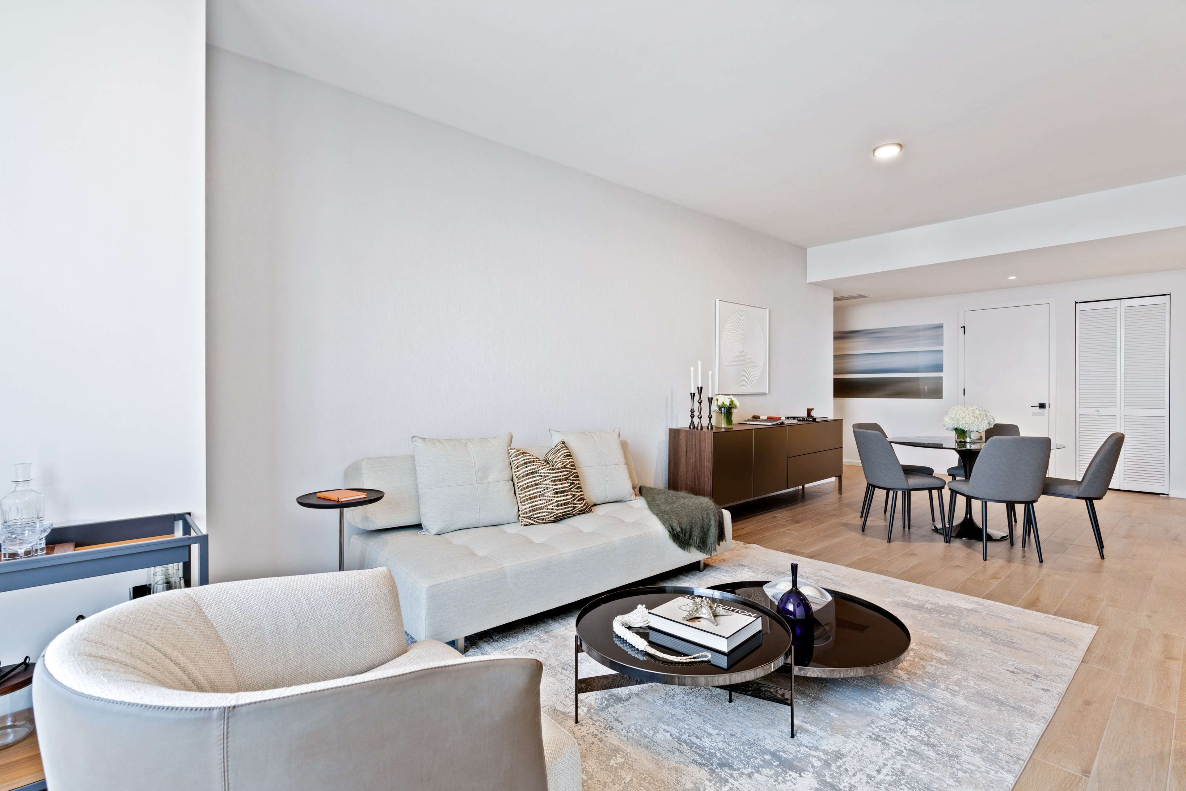 A modern living room with a sofa, armchair, coffee table, and dining area.