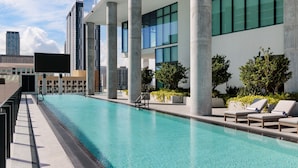 Una piscina moderna al aire libre con sillones de descanso y vistas a altos edificios.